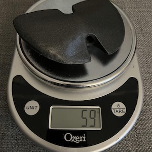 May include: A black Wu-Tang Clan logo, also known as the W symbol, is placed on a digital kitchen scale. The scale reads 59 grams.