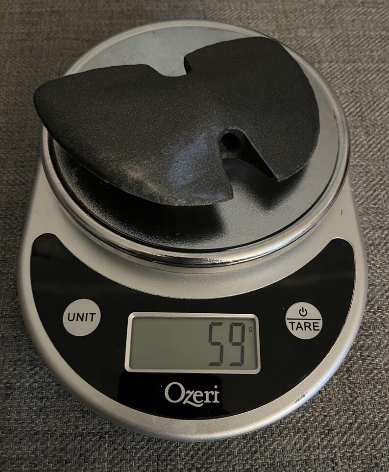 May include: A black Wu-Tang Clan logo, also known as the W symbol, is placed on a digital kitchen scale. The scale reads 59 grams.