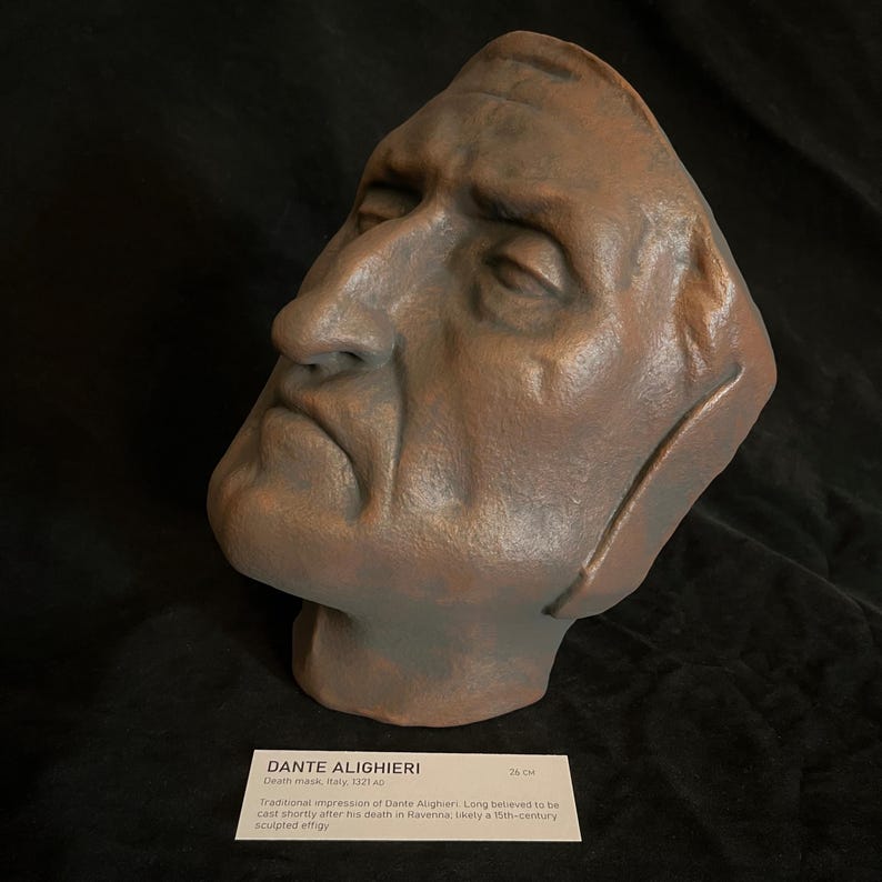 May include: A bronze-colored death mask of Dante Alighieri, with a somber expression. The mask is approximately 10 inches in length. A label below reads "DANTE ALIGHIERI Death mask, Italy, 1321 AD".