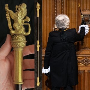 May include: A gold ceremonial staff featuring a lion figure. The staff is held by a person in a black coat with white lace cuffs, standing before a wooden door. The staff's total length is approximately 150 cm.