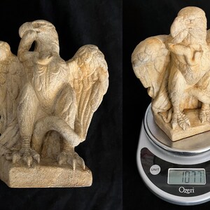 May include: A beige-colored griffin statue with outstretched wings and detailed feather textures. The sculpture is approximately 8 inches tall and is displayed on a digital scale, weighing 1077 grams.