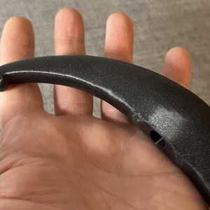 May include: Black plastic handle with a curved shape and a small hole in the centre.