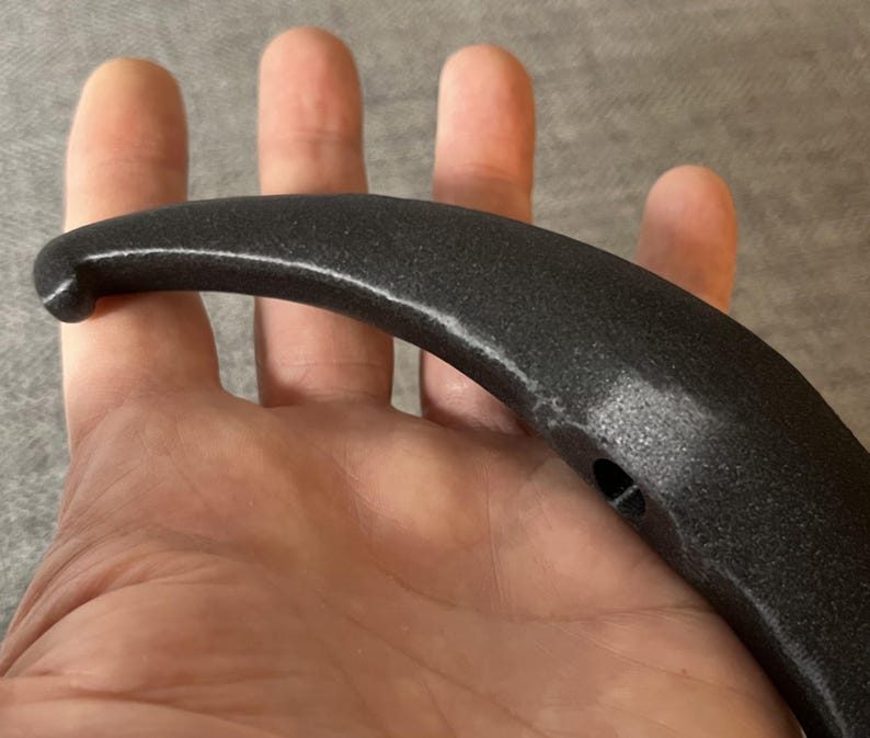 May include: Black plastic handle with a curved shape and a small hole in the centre.