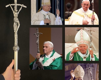 May include: A silver-colored processional cross with a detailed depiction of Jesus Christ on the cross. The cross is held by a person in the image. The image also shows several popes holding the same cross during religious ceremonies.