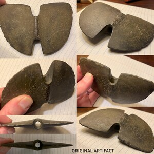 May include: A dark gray stone artifact with a unique shape, featuring a hole in the center and a split on one side. The artifact is likely an ancient tool or weapon.