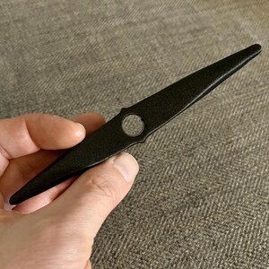 以下が含まれることがあります： 中央に穴が開いた先のとがった黒い金属製の道具。道具の長さは約25cmです。