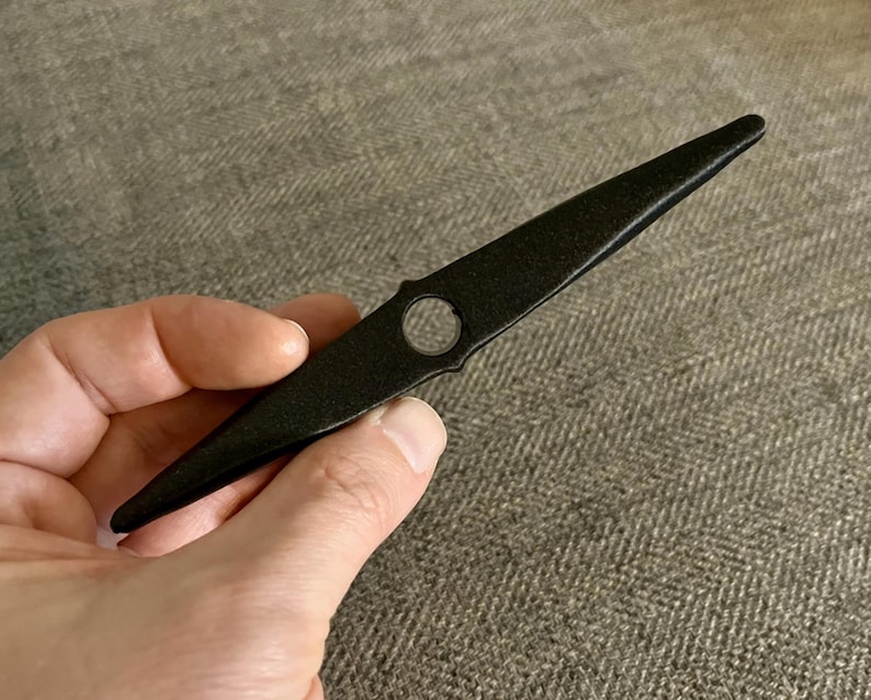以下が含まれることがあります： 中央に穴が開いた先のとがった黒い金属製の道具。道具の長さは約25cmです。
