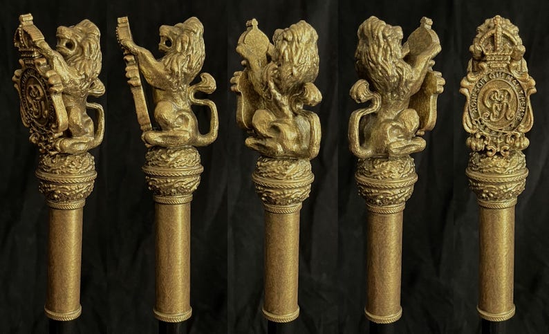 May include: Five antique gold-coloured walking stick handles. Each handle features a detailed lion sculpture atop a column-shaped shaft. The lion sculptures hold various emblems, including a shield and a crown, showcasing intricate craftsmanship.