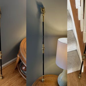 May include: A decorative walking stick with a black shaft and ornate gold-coloured metal accents. The top features a detailed sculpture. The stick is approximately 101.6 cm tall.