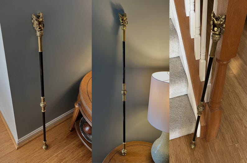 May include: A decorative walking stick with a black shaft and ornate gold-coloured metal accents. The top features a detailed sculpture. The stick is approximately 101.6 cm tall.