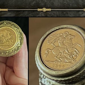 May include: An ornate walking stick with a gold-toned handle and detailing. The handle incorporates a gold coin with a rider on horseback, dated 1904. The shaft is silver-coloured, with decorative gold-toned elements.