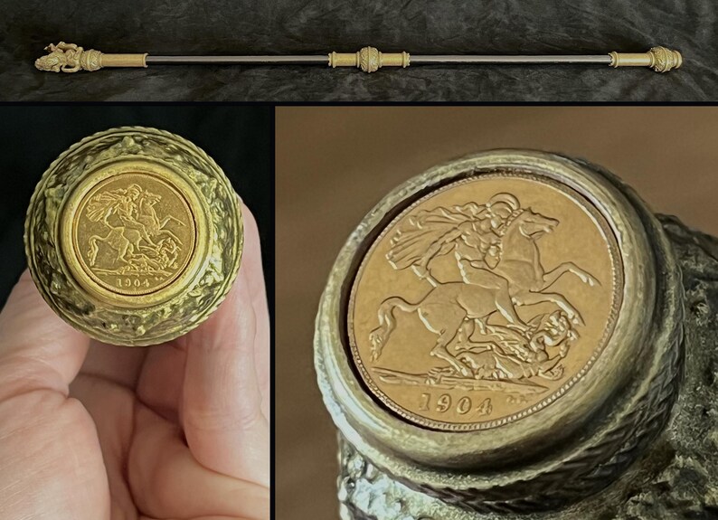 May include: An ornate walking stick with a gold-toned handle and detailing. The handle incorporates a gold coin with a rider on horseback, dated 1904. The shaft is silver-coloured, with decorative gold-toned elements.