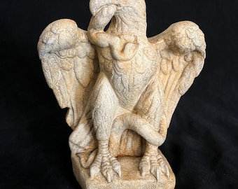 May include: A detailed, off-white eagle statue with outstretched wings and a thoughtful pose. The bird's talons are visible, and the statue is on a square base. The sculpture has a textured surface and is likely made of stone or a similar material.