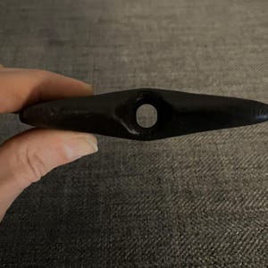 May include: A black, smooth, teardrop-shaped stone with a hole drilled through the center.