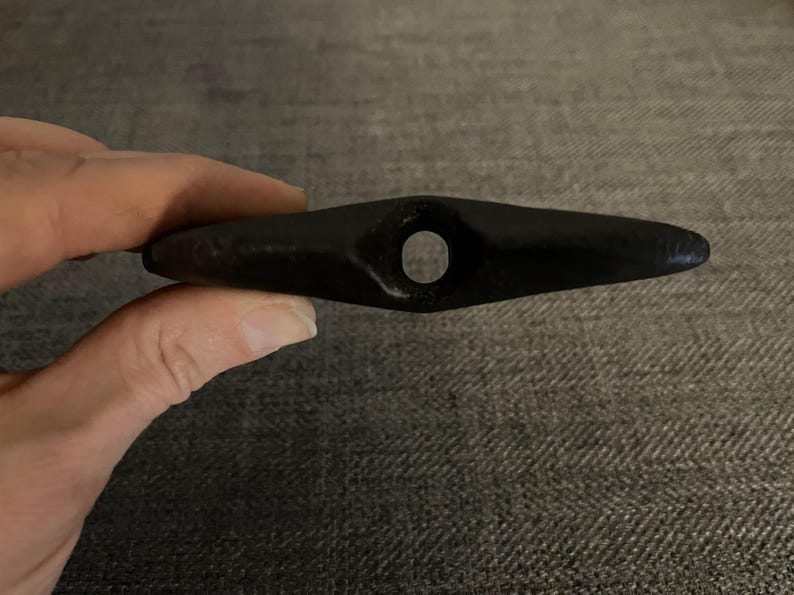 May include: A black, smooth, teardrop-shaped stone with a hole drilled through the center.