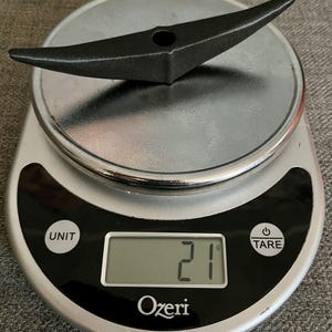 以下が含まれることがあります： 船のスクリューのような形の黒い金属製の物がデジタルキッチンスケールに乗っています。スケールは21グラムを示しています。