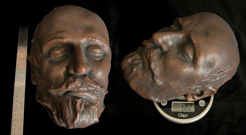 Puede incluir: Una escultura de color bronce de la cara de un hombre con los ojos cerrados y una barba completa. La escultura se muestra en dos vistas, una frontal y otra de perfil, con una regla para la escala. La vista de perfil descansa sobre una b&aacute;scula, con un peso de 188 gramos.