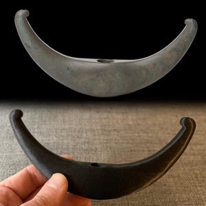 May include: A comparison of two crescent-shaped objects. The top object is a dark gray, smooth, and polished stone. The bottom object is a black, 3D printed replica of the stone.