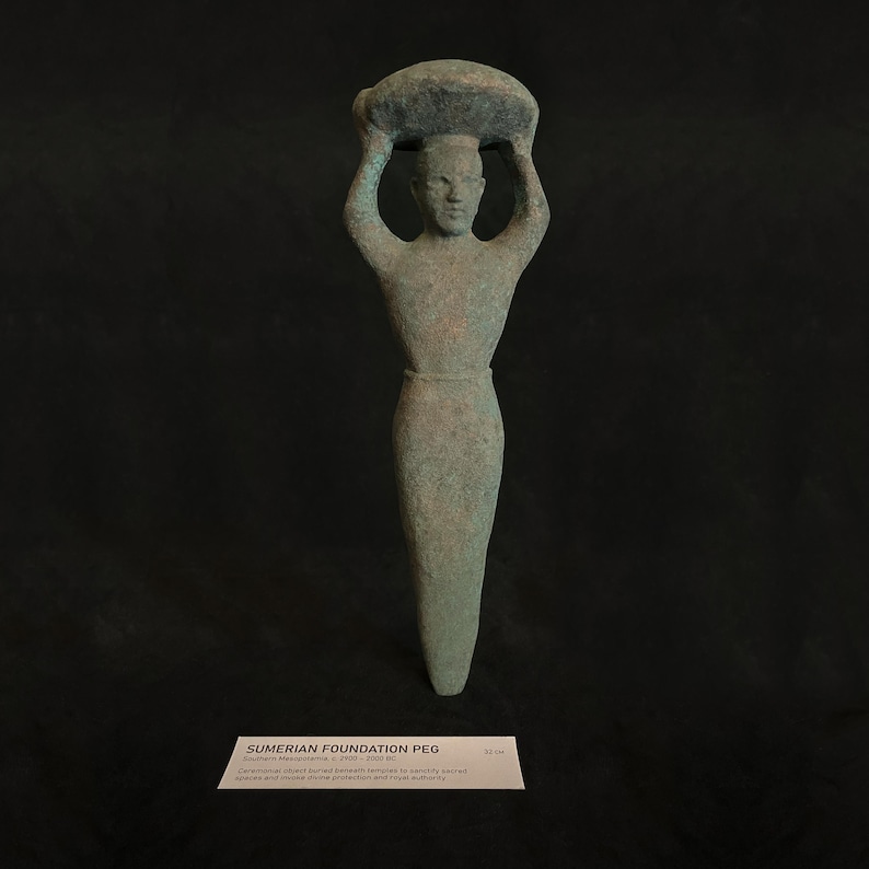 May include: A green bronze Sumerian foundation peg depicting a figure carrying a load on their head. The peg is 8.5 cm tall.  "Ceremonially placed buried beneath temples to symbolically ensure protection and royal authority."