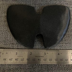 May include: A black rubber object shaped like a heart with a cutout in the middle. The object is measured with a ruler, showing it is about 1 inch wide.
