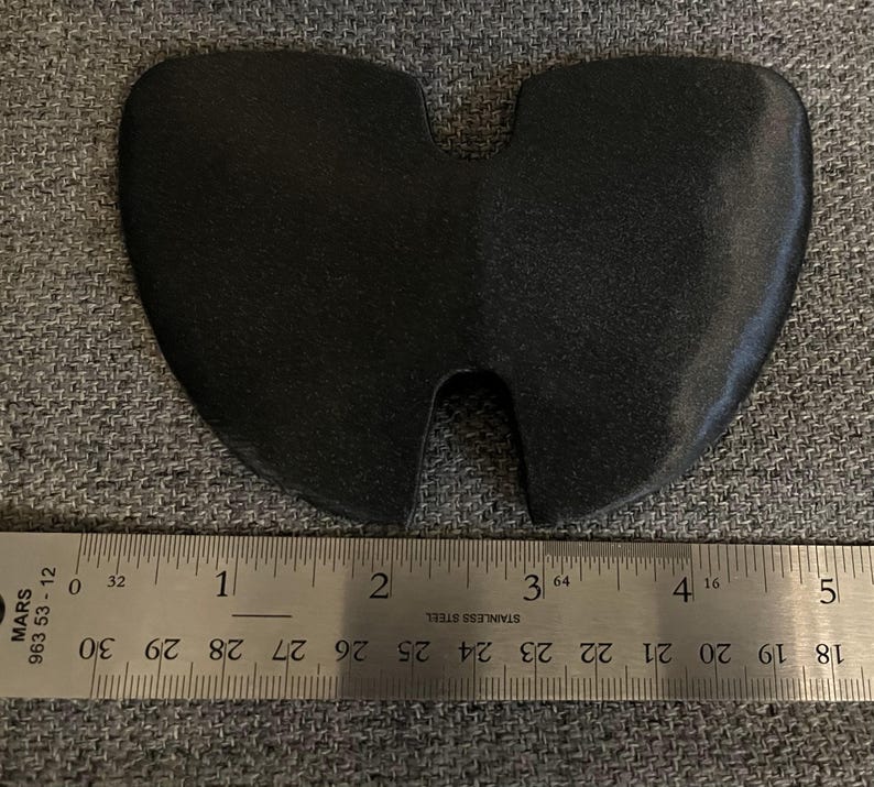 May include: A black rubber object shaped like a heart with a cutout in the middle. The object is measured with a ruler, showing it is about 1 inch wide.