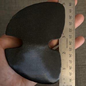 May include: A black, rubbery, three-hole, heart-shaped object, approximately 7 inches wide, measured against a ruler.
