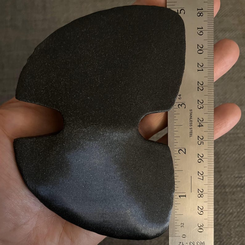 May include: A black, rubbery, three-hole, heart-shaped object, approximately 7 inches wide, measured against a ruler.