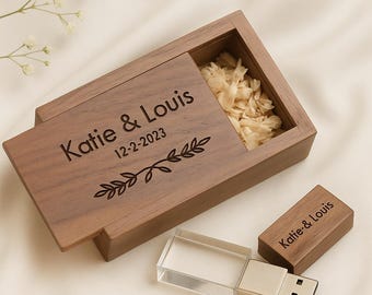 Op de afbeelding: Een houten USB-stick en bijpassende doos, beide gegraveerd met de namen "Katie & Louis", de datum "12-2-2023" en een bladontwerp. De doos is gedeeltelijk open en toont een compartiment gevuld met beige vulmateriaal.
