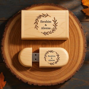 May include: A wooden USB flash drive and matching box, both engraved with the names "Ibrahim & Aleena" inside a laurel wreath design. The items are displayed on a wooden slice, with autumn leaves in the background.