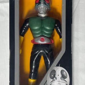 May include: A boxed Rider Hero Series action figure. The figure is in a clear plastic display case with a yellow background. The figure is green, black, silver, and red. The box has Japanese text and the Bandai logo.