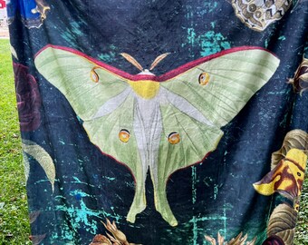 May include: A dark blue throw blanket with a large green and white luna moth, red roses, and other floral designs. The blanket has a vintage, distressed look.