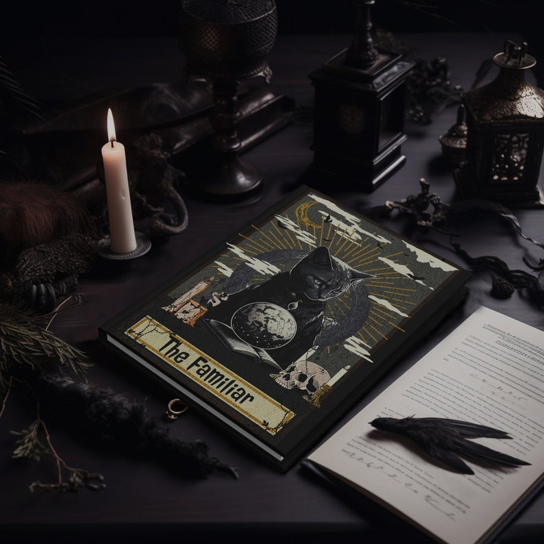 May include: A black leather journal with a gold and black illustration of a cat holding a globe and a skull. The journal has the text "The Familiar" on the front cover.