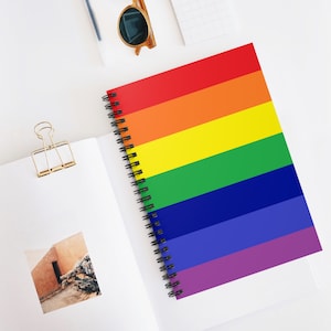以下が含まれることがあります： 虹色の旗のデザインが施された、スパイラルバインディングされたノート。表紙には、赤、オレンジ、黄、緑、青、紫の6本の水平なストライプがあります。
