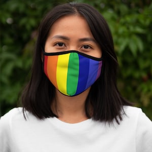 May include: A person wearing a face mask with a rainbow pattern. The mask is made of fabric and has a black elastic band.