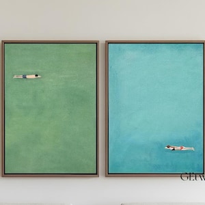 May include: Two framed wall art pieces depict swimmers in water. One canvas is green, the other is blue. The swimmers are small figures in the center of the artwork. The art is displayed above two white armchairs with wooden frames.