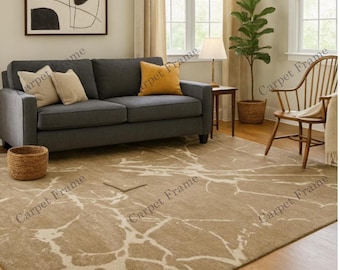 May include: A living room scene featuring a gray sofa with beige and yellow pillows, a wooden chair, and a large area rug. The rug has a beige background with white vein-like patterns. A framed abstract art piece hangs on the wall.