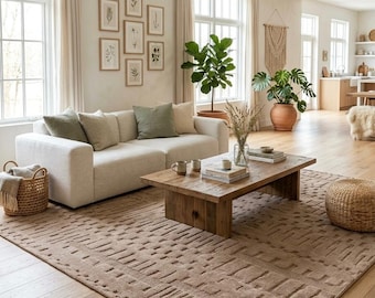 May include: A large rectangular area rug with a textured, raised geometric pattern in a solid tan color. The rug features a repeating block design across its surface, providing a tactile element to the floor space in a living room setting.