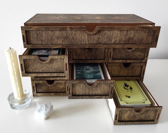 May include: Wooden box with a hinged lid and multiple drawers. The drawers are open and reveal tarot cards. The box is stained a dark brown color.