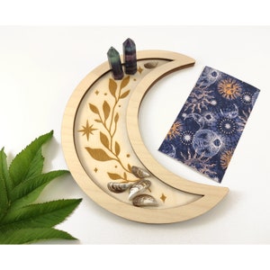 May include: A crescent moon-shaped wooden tray with a gold leaf design and stars. The tray is filled with seashells and crystals.