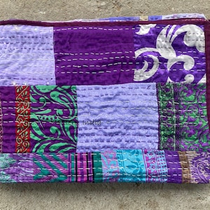 Puede incluir: Colcha de retazos morada y verde con un patrón floral. La colcha está hecha de saris reciclados y está cosida a mano. "Ghost of a Mystery" India está escrito en la colcha.