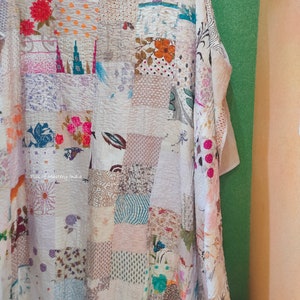 Puede incluir: Una colcha de retazos hecha de varias telas con patrones florales y geométricos en tonos de rosa, azul, marrón y blanco. La colcha está colgada en una pared.