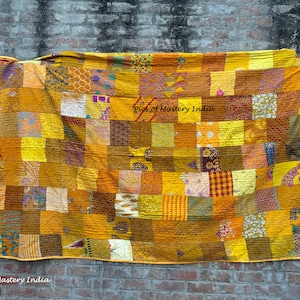 May include: A patchwork quilt with a variety of yellow, gold, and brown fabric squares. The quilt is hanging against a brick wall. The text "Pics of Mastery India" is visible in the lower left corner.