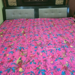 May include: A pink kantha quilt with a floral and bird pattern. The quilt is made of cotton and has a hand-stitched design. The quilt is perfect for adding a touch of bohemian style to any bedroom.