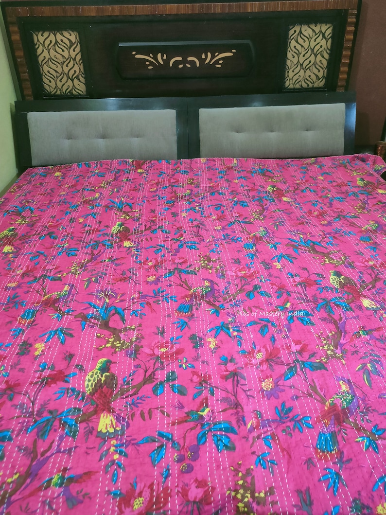 May include: A pink kantha quilt with a floral and bird pattern. The quilt is made of cotton and has a hand-stitched design. The quilt is perfect for adding a touch of bohemian style to any bedroom.