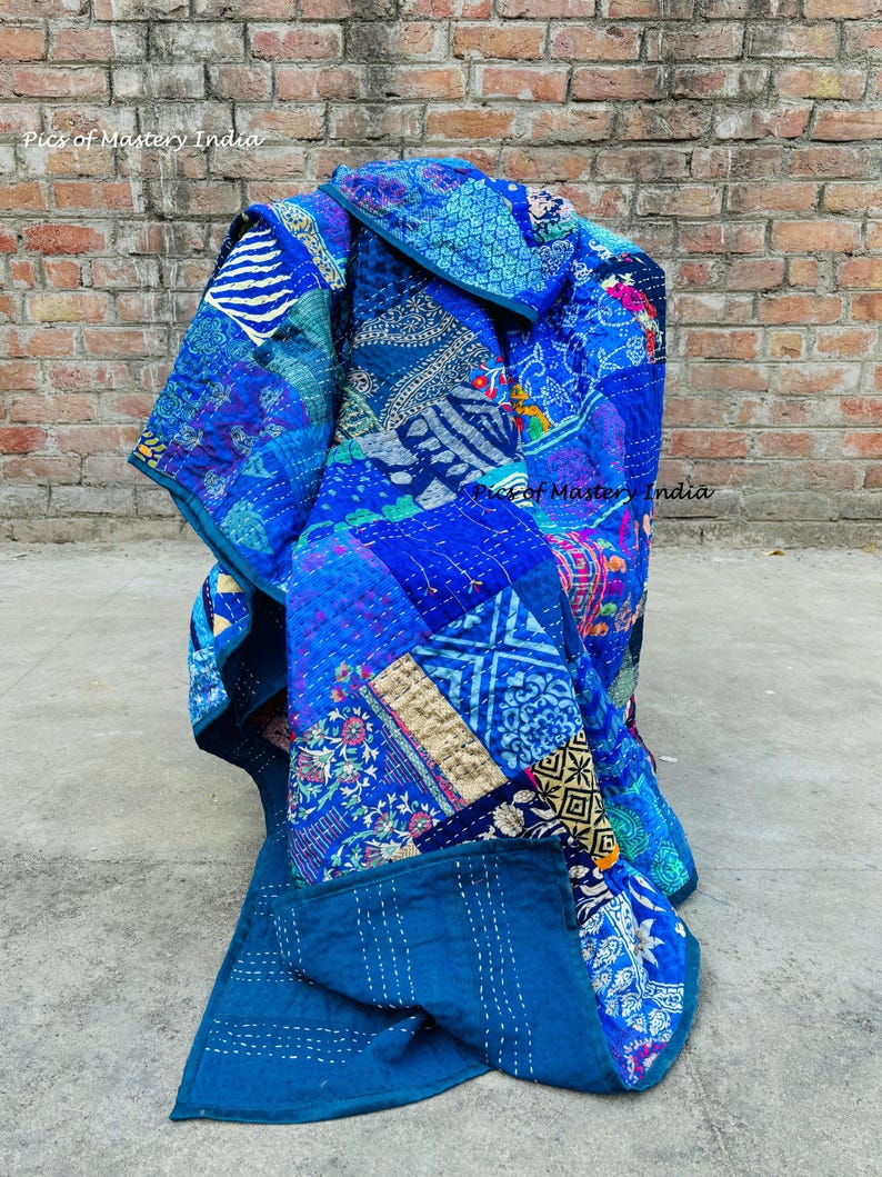 May include: A vibrant blue patchwork quilt with various patterns and textures. The quilt features a mix of floral, geometric, and abstract designs in shades of blue, teal, and indigo. The text "Pics of Mastery India" is visible.