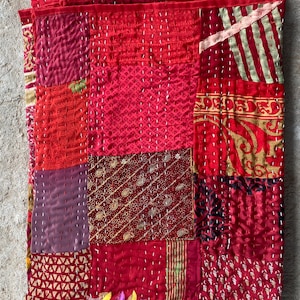 Puede incluir: Una colcha de retazos roja y dorada con puntadas intrincadas. La colcha está hecha de varias telas con diferentes patrones y texturas.