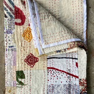 May include: A white patchwork quilt with red stitching and a variety of patterns, including floral, geometric, and polka dots. The quilt is folded in half and has a white border.