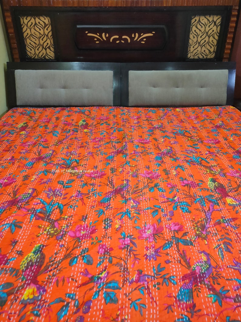 May include: Orange kantha quilt with a floral and bird pattern. The quilt is made of cotton and has a hand-stitched design.