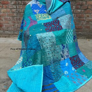 May include: A patchwork quilt in shades of teal, turquoise, and blue, with a solid turquoise backing. The quilt features a variety of patterned fabrics, including floral and geometric designs, stitched together with white thread. The quilt is draped over an unseen object.