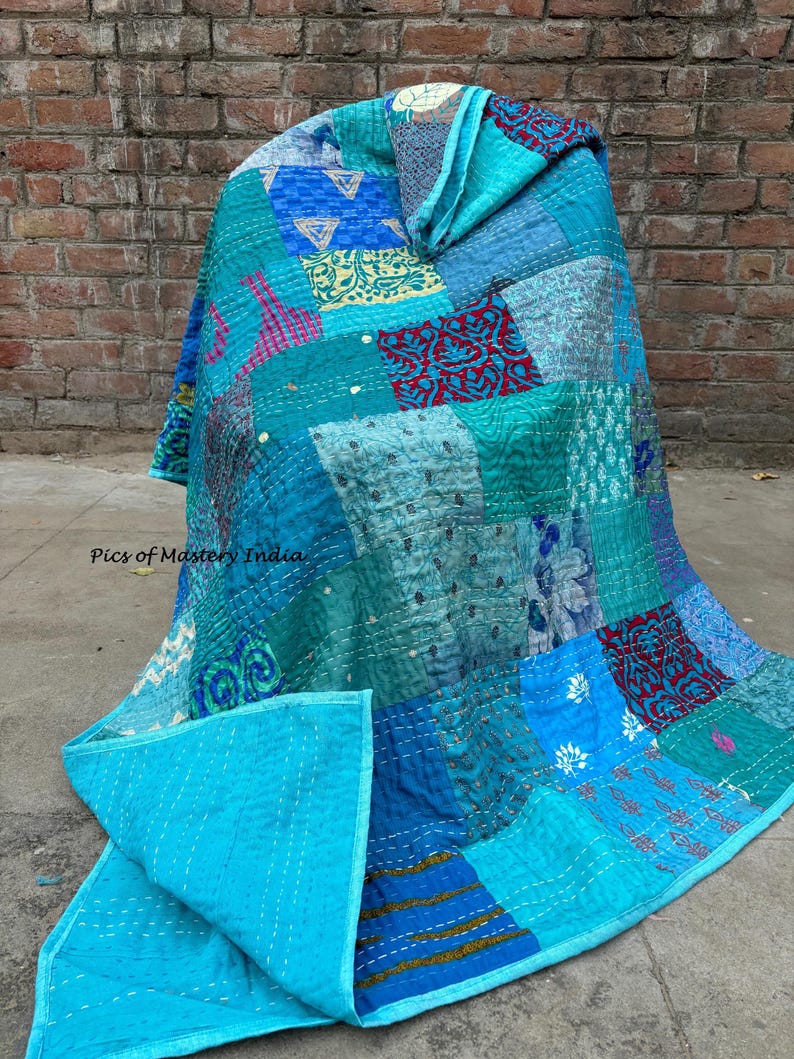 May include: A patchwork quilt in shades of teal, turquoise, and blue, with a solid turquoise backing. The quilt features a variety of patterned fabrics, including floral and geometric designs, stitched together with white thread. The quilt is draped over an unseen object.